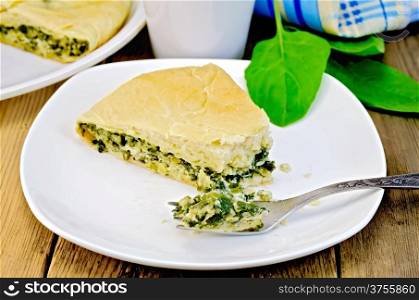 Pie with spinach and cheese on a plate, spinach leaves, mug, fork, napkin on wooden board