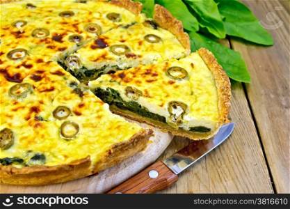 Pie with spinach, cheese and olives on a round board, spinach leaves, knife, napkin on wooden board