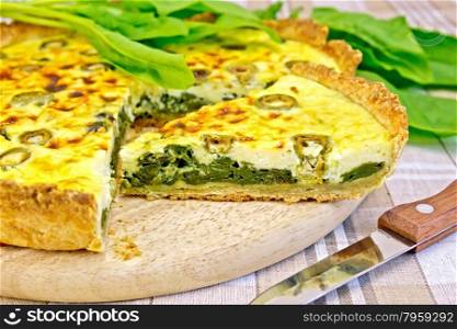 Pie with spinach, cheese and olives on a round board, spinach leaves, knife on background linen tablecloths