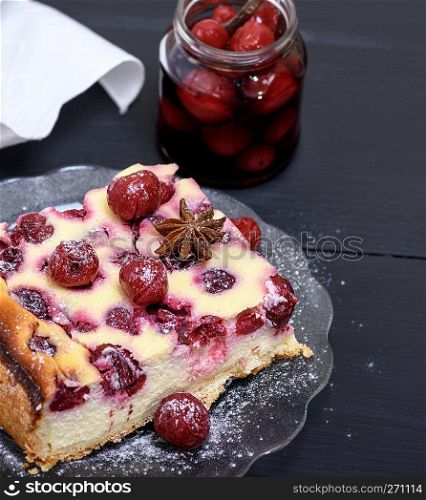 piece of a cheesecake with cherries on a glass plate and a jar with  berries