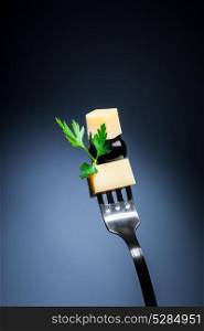 Piece of cheese with black olive and parsley on the fork over dark background, healthy and tasty nutrition, dieting concept