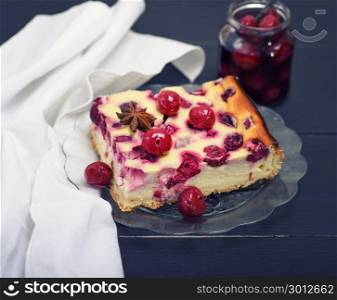 piece of cheesecake with cherry berries on a glass plate, behind a jar of canned cherries