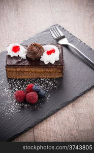 Piece of chocolate cake with berries on dark slate tray.