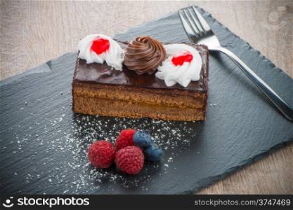 Piece of chocolate cake with berries on dark slate tray.