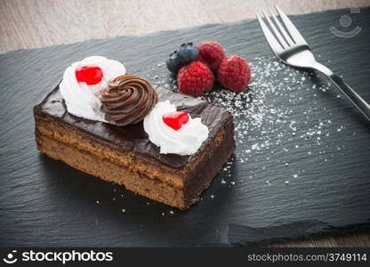 Piece of chocolate cake with berries on dark slate tray.