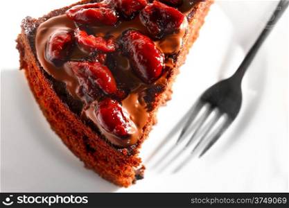 Piece of chocolate cake with icing and cherry on white background