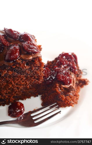 Piece of chocolate cake with icing and cherry on white isolated background