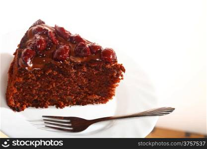 Piece of chocolate cake with icing and cherry on white plate