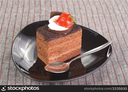 Piece of Chocolate cake with strawberry in black plate on the table