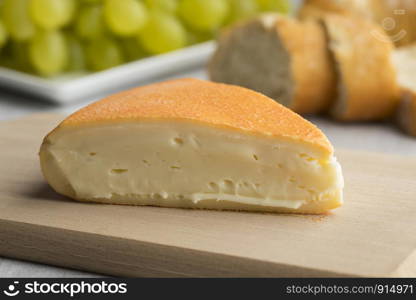 Piece of creamy French Chaumes cheese on a cutting board close up