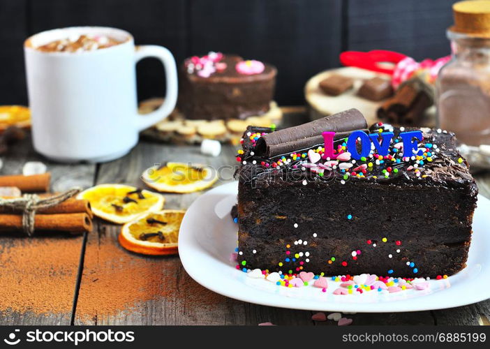 piece of festive chocolate cake strewn with a multicolored powder, behind a cup with a drink