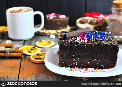 piece of festive chocolate cake strewn with a multicolored powder, behind a cup with a drink