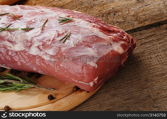 piece of fresh raw meat on cutting board with rosemary