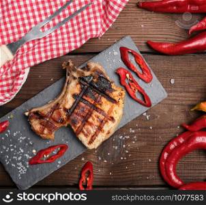 piece of fried pork tenderloin on a bone lies on a black board, juicy meat, close up