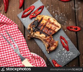 piece of fried pork tenderloin on a bone lies on a black board, juicy meat, close up