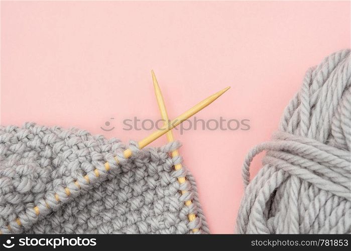 Piece of grey knitted fabric on bamboo wood needles with ball of yarn, process of knitting on pink background. Copy space for text .Top view Flat lay Template for your design.. Piece of grey knitted fabric on bamboo wood needles with ball of yarn, process of knitting on pink background. Copy space for text .Top view Flat lay Template for your design