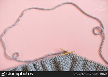 Piece of grey knitted fabric on the needles, process of knitting on pink background. Copy space for text .Top view Flat lay Template for your design.. Piece of grey knitted fabric on the needles, process of knitting on pink background. Copy space for text .Top view Flat lay Template for your design