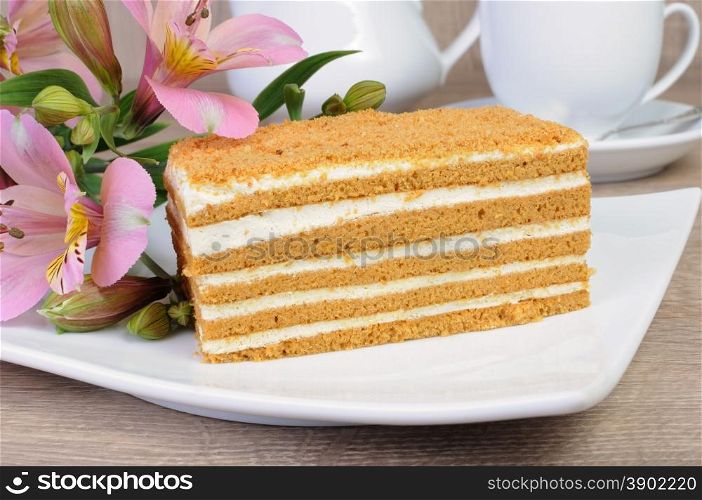 Piece of honey cake with a cup of coffee on a table with a flower
