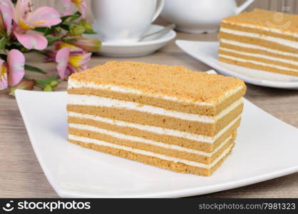 Piece of honey cake with a cup of coffee on a table with a flower