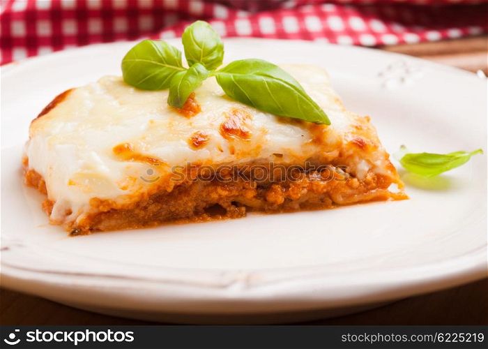 Piece of lasagna bolognese with basil leaves in a white plate. Classic lasagna bolognese