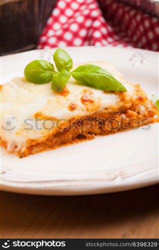 Piece of lasagna bolognese with basil leaves in a white plate. Classic lasagna bolognese