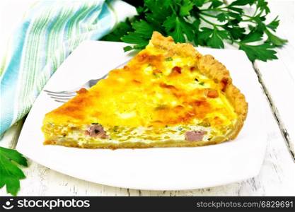 Piece of pie kish with pumpkin and bacon, filled with milk with eggs and cheese in a plate, parsley, a towel on the background of a light wooden board