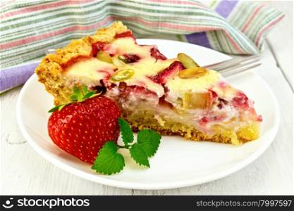 Piece of pie with strawberries, rhubarb and cream sauce, fork, strawberries and mint in white plate, napkin on a wooden boards background