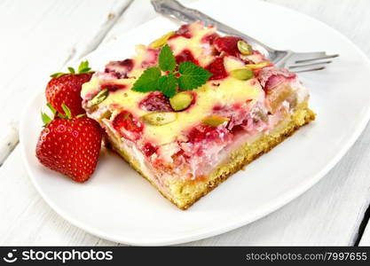 Piece of pie with strawberries, rhubarb and cream sauce, fork, strawberry, mint in white plate on a wooden boards background