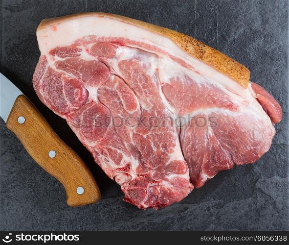 Piece of pork meat and ax on the black stone table