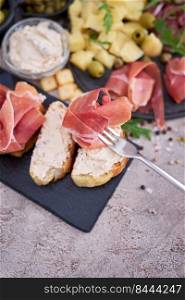 piece of prosciutto ham on a fork with traditional antipasto meat plate on background.. piece of prosciutto ham on a fork with traditional antipasto meat plate on background