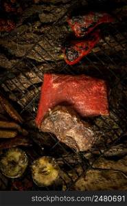 piece of raw meat with vegetables on the grill on a background of tree bark. dish on a tree bark