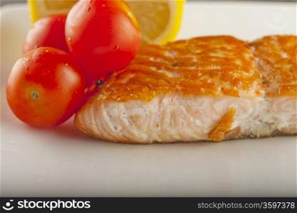 Piece of salmon over a white plate, with tomatoes and lemon