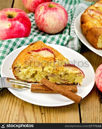 Piece of sweet apple pie, cinnamon, napkin, fork, apples on a wooden boards background