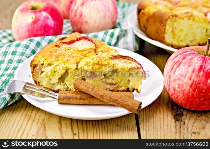 Piece of sweet apple pie, cinnamon, napkin, fork on the background of wooden boards