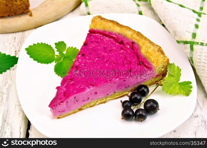 Piece of sweet cake with black currants and mint in a plate, napkin against the background of wooden boards
