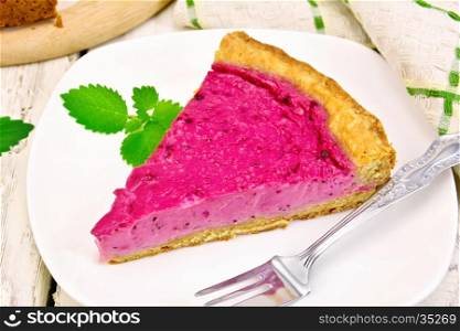 Piece of sweet cake with black currants, blueberries or blackberries, mint and fork in a plate, napkin against the background of wooden boards