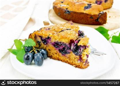 Piece of sweet cake with black grapes and honey, mint and a fork in a plate, a towel on light wooden board background