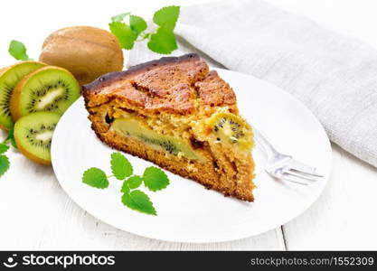 Piece of sweet cake with kiwi and honey, mint and fork in a plate, napkin on a wooden board background