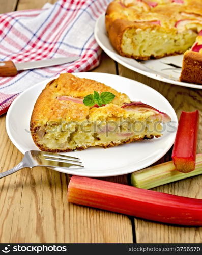 Piece of sweet cake with rhubarb, mint, napkin, knife, fork on the background of wooden boards