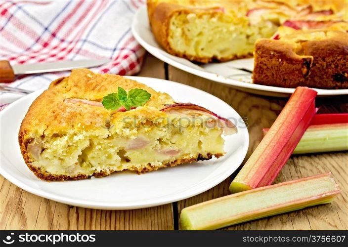 Piece of sweet cake with rhubarb, mint, napkin, knife on background wooden plank