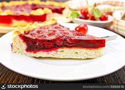 Piece of sweet pie with cherries and jelly in a plate with a fork on the background of wooden boards