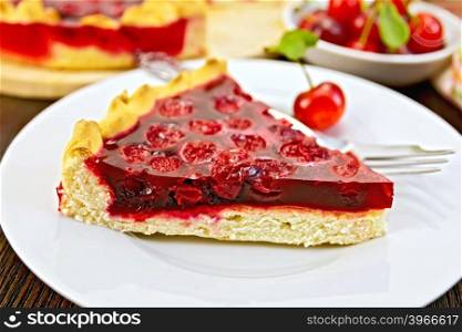 Piece of sweet pie with cherries and jelly in a white plate with a fork on the background of wooden boards