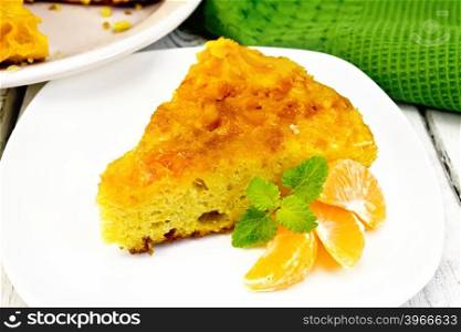 Piece of tart with mandarin, mint, mandarin slices in a white plate, towel on a background of wooden boards