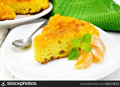 Piece of tart with mandarin, mint, tangerine slices and spoon in white plate, towel on a background of wooden boards