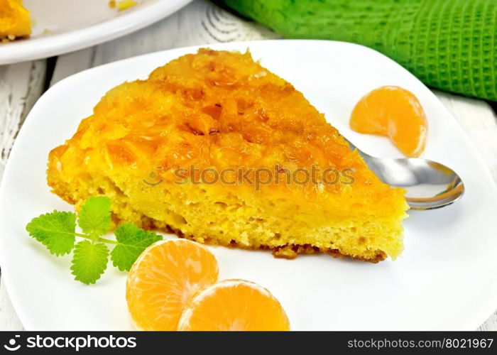 Piece of tart with mandarin, mint, tangerine slices and spoon in white plate, a towel on the background light wooden boards