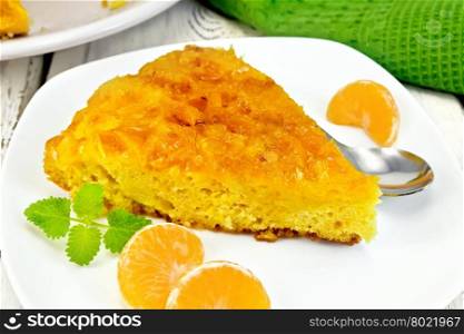 Piece of tart with mandarin, mint, tangerine slices and spoon in white plate, a towel on the background light wooden boards