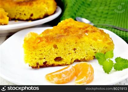 Piece of tart with mandarin, mint, tangerine slices in white plate, a towel and a spoon on a background of wooden boards