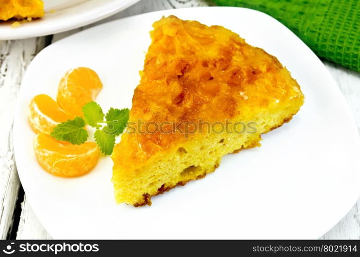 Piece of tart with mandarin, mint, tangerine slices in white plate, a towel on the background light wooden boards