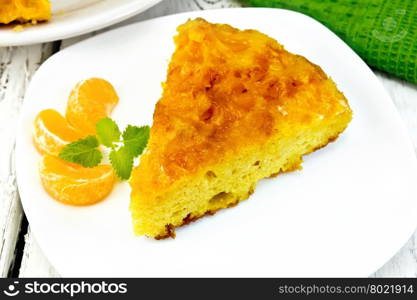 Piece of tart with mandarin, mint, tangerine slices in white plate, a towel on the background light wooden boards