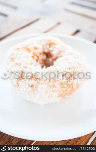 Piece of vanilla coconut donut on white plate, stock photo